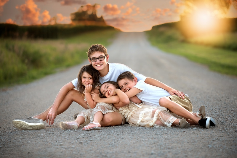 NE Family Photographer, four siblings sitting together on a dirt road